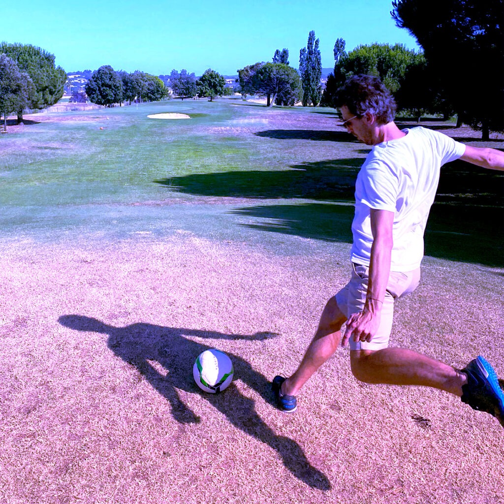 A man is kicking a soccer ball on a golf field